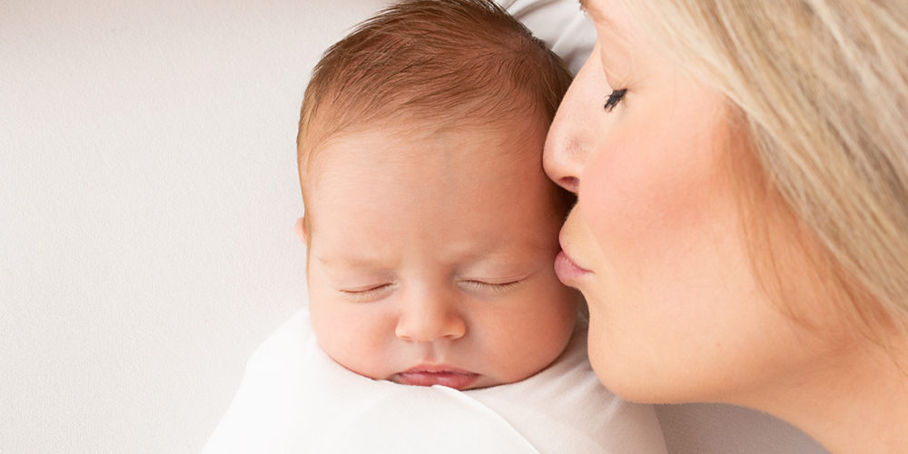 Mum kissing baby girl during newborn photoshoot in Woking