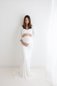 Maternity photoshoot in Woking pregnant woman in white gown looking down at belly