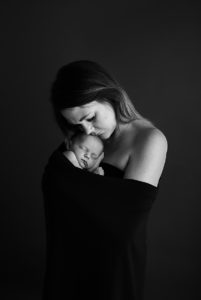 Black and white of mum cradling her newborn baby girl in her arms during newborn photoshoot in Woking, Surrey