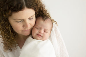 Mum holding her baby girl and looking down at her. Baby girl smiling during newborn photoshoot in Woking